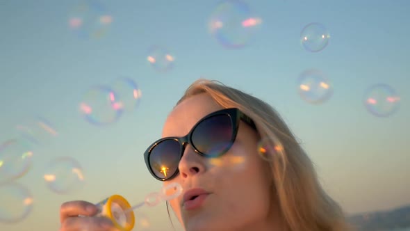 Young Woman in Sunglasses Blowing Soap Bubbles