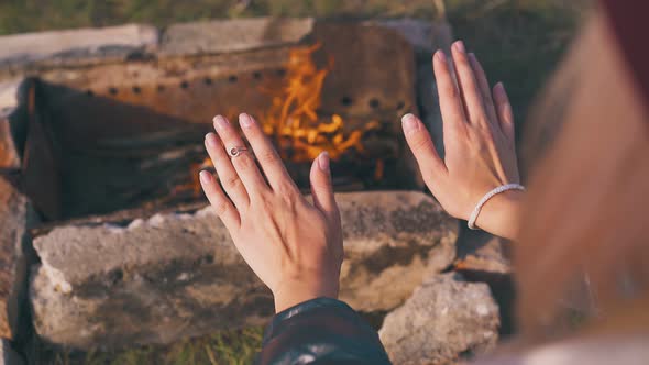 Young Lady Heats Palms at Burning Bonfire in Autumn Morning