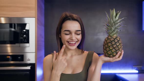 Brunette Holding in Her Hand Pineapple and Making Sign "it's Good Choice" on the Kitchen Background