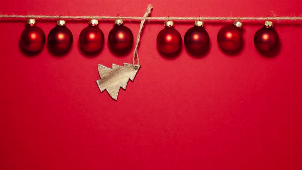 Red christmas balls on thread and in the middle is a wooden Christmas tree on the top side alt