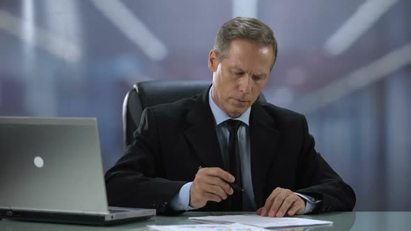 Serious Businessman Reading and Signing Important Contracts at Office Desk