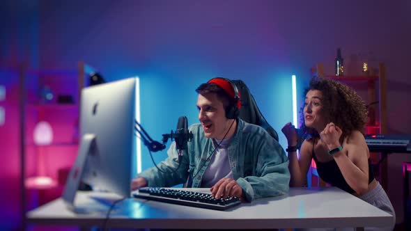 Excited Gamer Guy and Young Woman Wearing Headphones Playing Computer Game Neon Fashion Room Winner