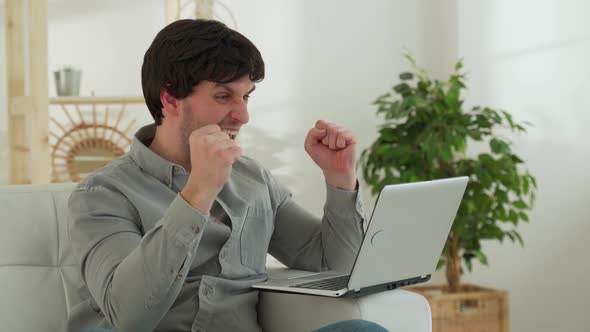 Happy Man Working at Computer at Home and Celebrating Victory Reads Good News By Email with Raised