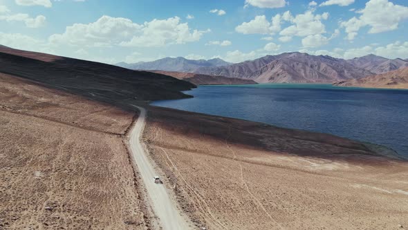 Aerial Over Off Road 4X4 Car Driving Along Gravel Trail Path Toward Lake in Arid Mountains