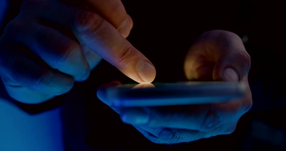 Man Is Scrolling Display of Smartphone, Browsing Internet at Night, Closeup View of Fingers