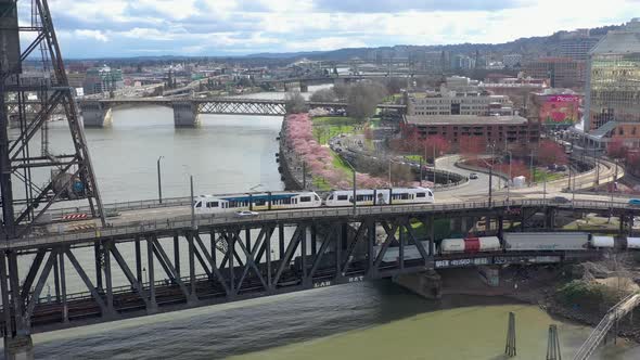 Flying toward cherry blossom trees as train passes over Steel Bridge in Portland Oregon.