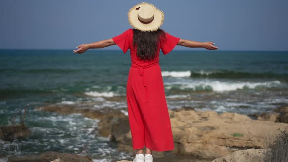 Back View Young Excited Woman in Red Dress Standing on Mediterranean Sea Beach Raising Hands in Slow