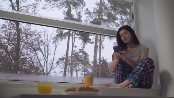 Female Holding Mobile Sit on Windowsill