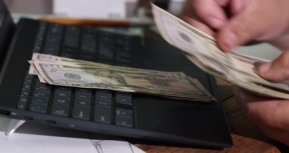 Hands of Man Accountant Counting Dollar Banknotes with Writes the Result to the Note Laptop