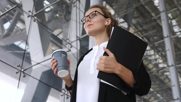 Stylish Business Woman With Coffee Wearing Bluetooth Earphones