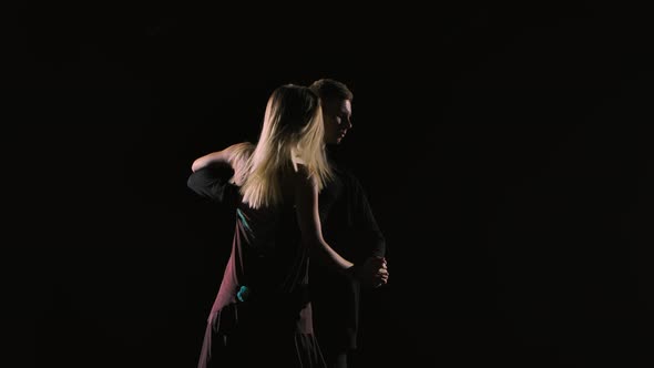 Couple of Ballroom Dancers Perform Bachata Dance Element on Black Studio Background in Darkness