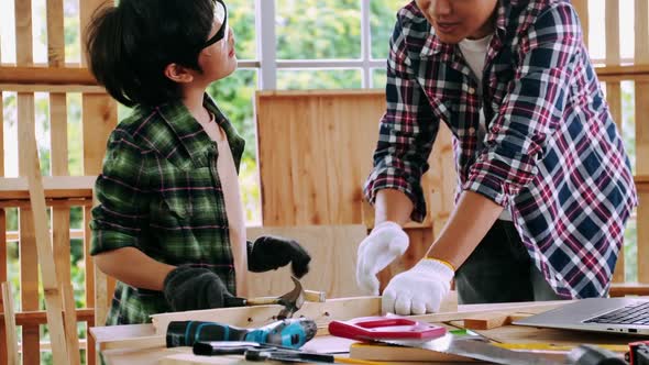 Carpenter Asian man teaching his son how to work with wood in workshop.