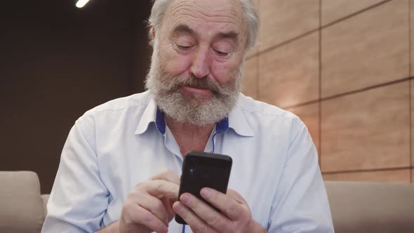 Happy bearded senior elderly 70s man user holding smart phone watching mobile video calling online l