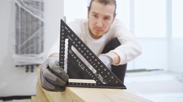 Carpenter in Protective Gloves Makes Measurements Using a Triangle on Wood
