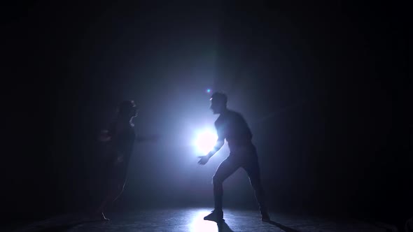 Silhouette of Couple Dancers Against Spotlight with Haze at Dark Studio.