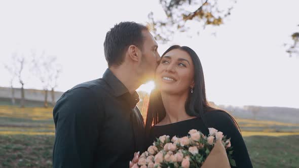 A Smiling Positive Young Couple in Love with a Man and a Woman Embrace While Sitting in Nature at