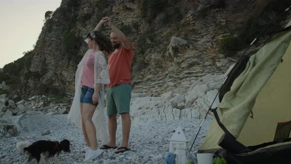 Young pretty woman and man dancing together on pebble beach near the sea on sunset