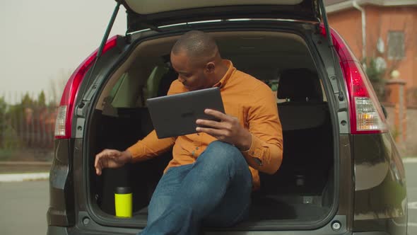 Relaxed Man Using Tablet Pc While Sitting in Car Trunk