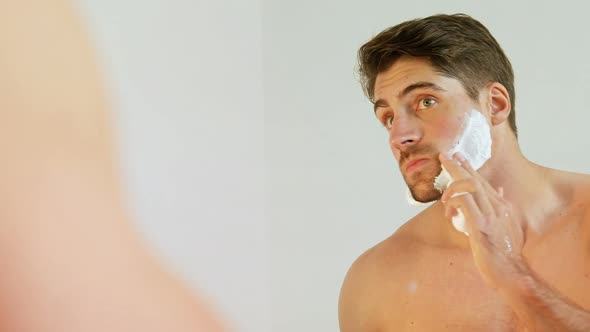 Young man looking into mirror applying shaving foam on his face 4K 4k