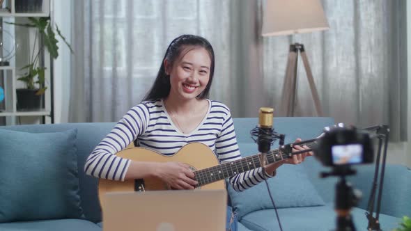 Asian Woman With A Laptop Holding A Guitar And Smiling To Camera While Live Stream At Home