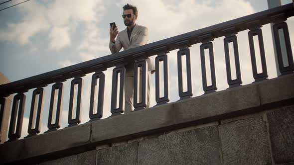 Businessman Stands On Bridge And Talking On Mobile Phone.Freelancer Cellphone Calling Online Meeting