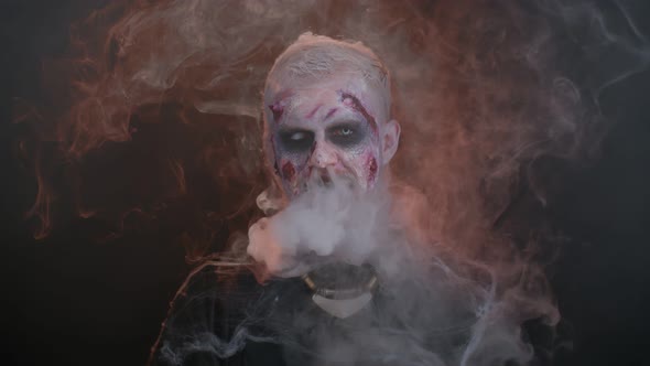 Sinister Man Horrible Scary Halloween Zombie Looking Ominous at Camera Blows Smoke From Nose Mouth