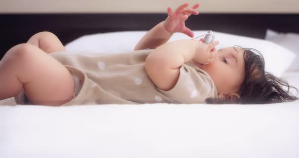 Baby Girl Lies on a Bed in the Nursery Plays and Chewing Foot