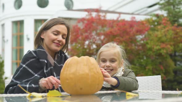 Mother Helping Daughter to Carve Pumpkin Jack for Halloween School Competition