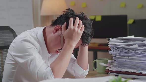 Close Up Of Asian Man Having Headache While Working Hard With Documents At The Office