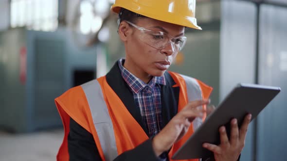 Negatively surprised African woman engineer in uniform checking something on tablet