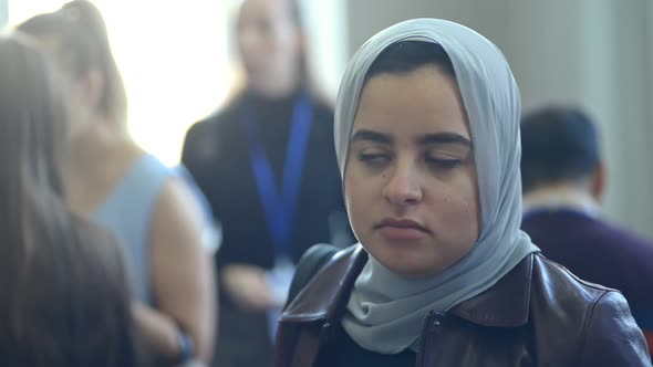 Muslim Woman Listening to Colleagues Friends Talking in Conference Hall with People Passing Irrl