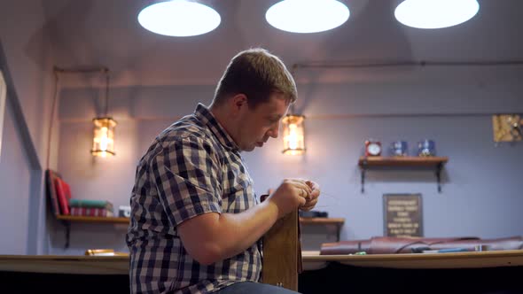 A Man in a Plaid Shirt Stitches Thread Leather Pieces. He Creates a Purse for Individual Design in