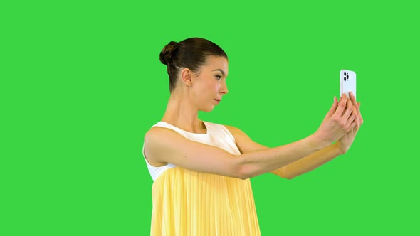 Young Beautiful Girl in Whiteyellow Dress Stands and Takes a Selfie on a Green Screen Chroma Key