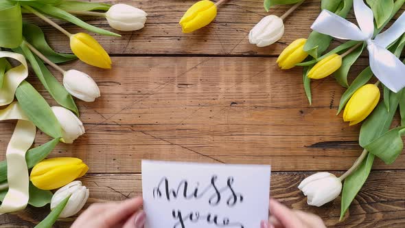 Put a card MISS YOU on a wooden table between tulips top view