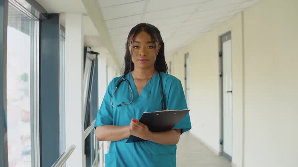 A Young African American Female Doctor in a Blue Suit Stands in the Corridor of the Clinic and