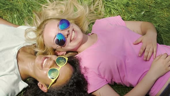 Two Beautiful Women Lying on Green Lawn, Talking, Enjoying Holidays Outdoors