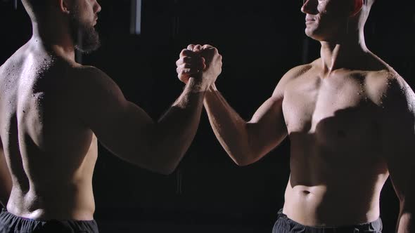 Two Focused Topless Men Shake Hands Amidst the Raindrops and Splashing Water. Picture Taken in the