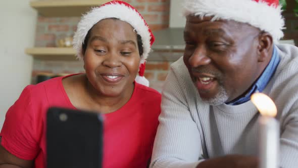 Happy african american senior couple in santa hats with presents on video call at christmas time