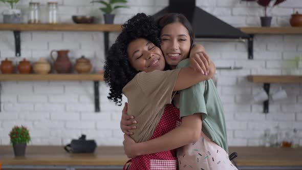 Live Camera Approaches to Happy Smiling African American and Asian Women Hugging in Kitchen