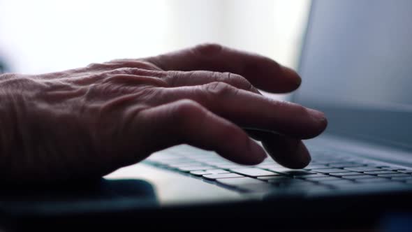 Elderly person online theme. Close-up of a senior's hand is typing text on a laptop keyboard. An eld