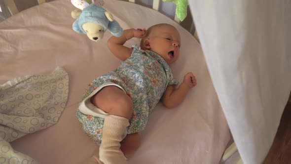 Baby with Hiccup Lying in Crib with Toy Mobile