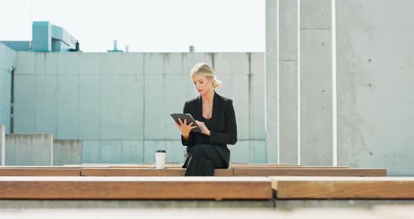 Young and Beautiful Caucasian Woman Using Her Tablet PC While Sitting on Bench Outside the