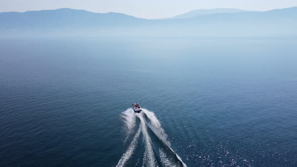 Speed boat driving fast in curves over deep, blue Okanagan Lake on a hot summer day in Canada. High