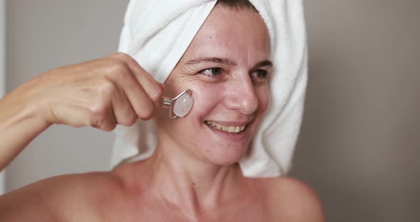 Caucasian mature woman using natural rose quartz skin care roller for her face - Beauty day concept