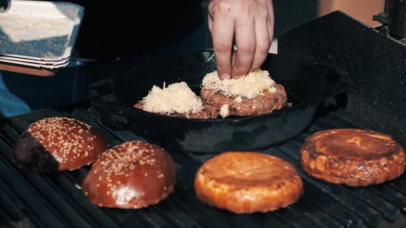 Frying patties and burger buns in a frying pan and grill, man adding cheese. BBQ