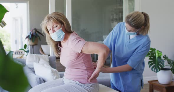 Female health worker stretching back of senior woman at home