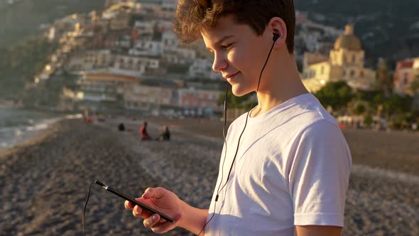 Teenage Boy Listening To Music Through His Smartphone and Relaxing on the Beach, Happy Boy in White