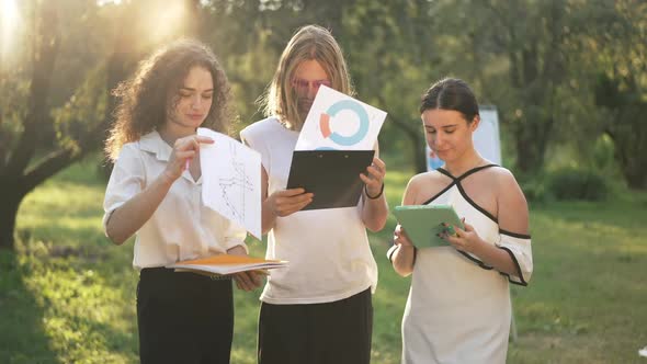 Three Confident Smart Colleagues Analyzing Paperwork and Emarket Looking at Camera Smiling