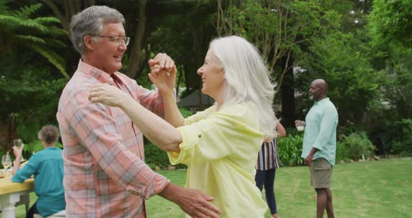 Animation of happy caucasian senior couple danging in garden while having lunch with friends