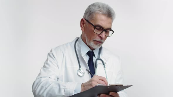 Elderly Doctor Therapist in Glasses and Medical Gown with a Stethoscope Makes Notes in Tablet White